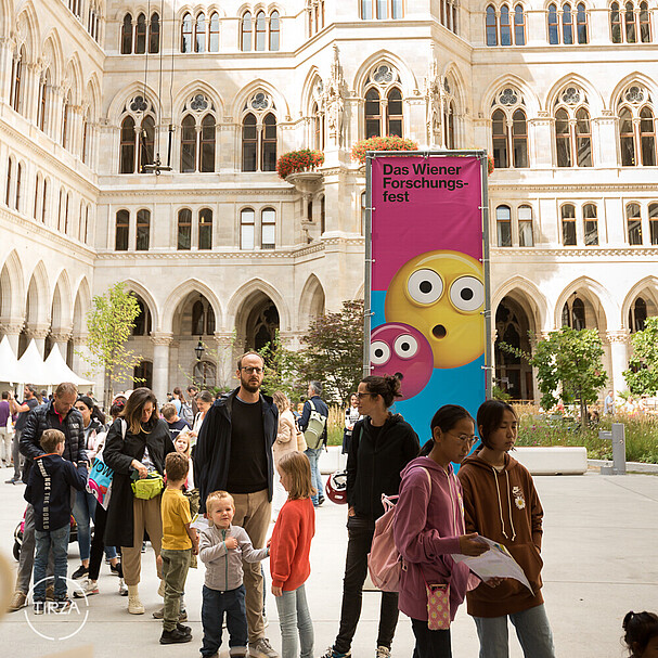 A queue of children and parents outside Vienna's city hall in front of a colourful poster which reads 'Das Wiener Forschungsfest'