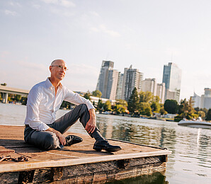 Man in white shirt sitting casually at pier and looking at the Donau